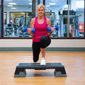 Woman exercising with blue dumbbells on a step platform in a gym.