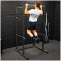 Person using a pull-up bar on a black metal power rack against a black brick wall.